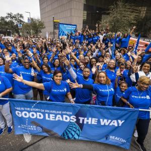 A large group of people wearing blue stand behind a blue parade banner with the words, "good leads the way" written in white