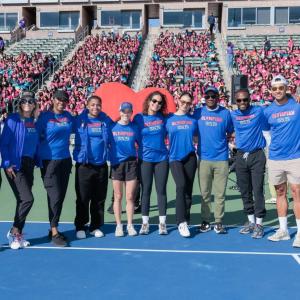 Olympians and Paralympians wearing blue “Olympian Ready, Set, Gold!” shirts pose for a group photo on the field in front of a stadium crowd of girls attending Girls Empowerment Day.