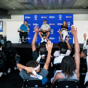 Panel discussion on stage at an LA Galaxy event as youth attendees raise their hands to ask questions.