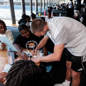 LA Galaxy Defender Chris Rindov signs items while children sit around a table during a hands-on activity session.