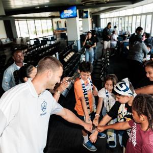 An LA Galaxy Defender Chris Rindov leans in to fist bump a group of kids gathered around a table in a stadium suite.