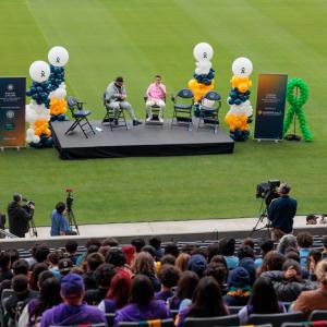 An outdoor audience watches people seated on a stage