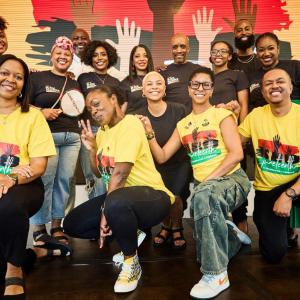 A group of Black men and woman, five wearing yellow t-shorts and ten wearing black t-shirts