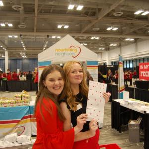 Two people posing in front of Nourishing Neighbors booth