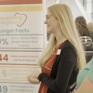 Two people talking in front of Nourishing Neighbors sign with hunger facts