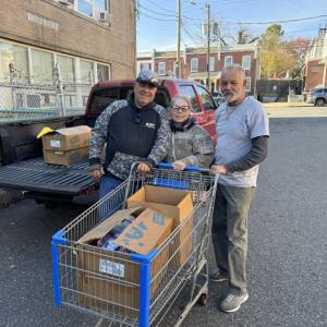 Three people pushing a grocery cart with boxes in it