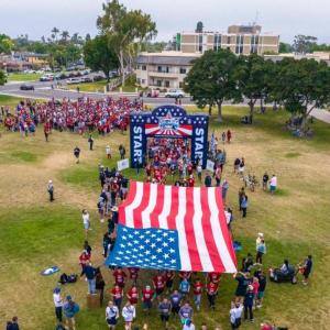People holding a large American flag on a field  