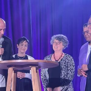 People collected together on a stage around a wooden table