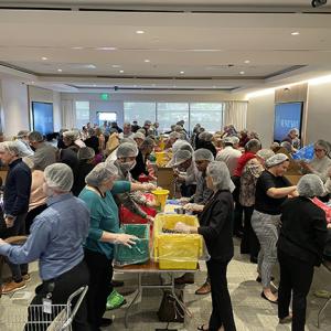 A room full of people in hair nets packing boxes on tables