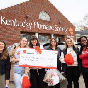 Six people standing together outside in front of the Kentucky Human Society, holding a large check