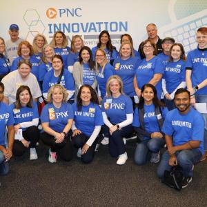 A group of people in blue t-shirts posed in front of a wall: "PNC Innovation"