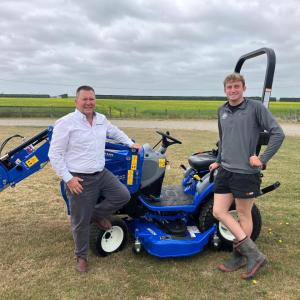 Two people standing in a field next to a blue tractor
