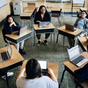 A group of people sat at desks in a circle using laptops