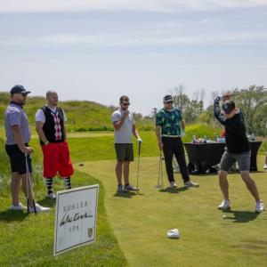 People standing on a green watching someone golfing