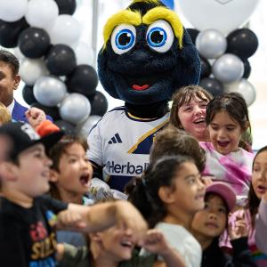 The LA Galaxy mascot stands among a group of children in front of black, white and silver balloons and LA Kings signage.