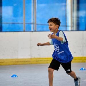 A child wearing a blue LA Galaxy training vest runs across an indoor court during a youth sports activity.
