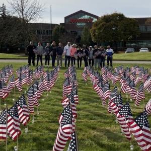Group of people posing behind field with flags in front of Albertsons Cos' Shaw's Store Support Center Sign