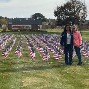 Two people posing in front of field with flags in front of Albertsons Cos' Shaw's Store Support Center Sign