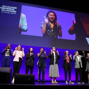 11 people standing in a row on stage.