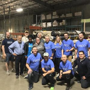 A group of people posed in a warehouse, many wearing matching Cisco t-shirts.
