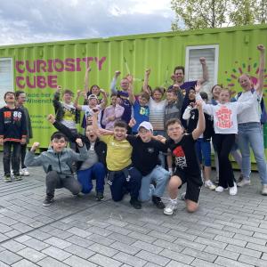 A class of students pose outdoors with MilliporeSigma employees behind the Curiosity Cube shipping container.