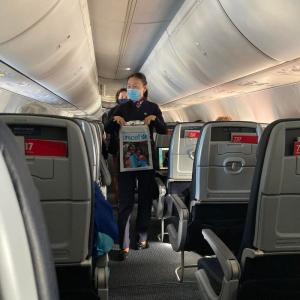 Flight attendant walking down an airplane aisle holding a UNICEF donation bag