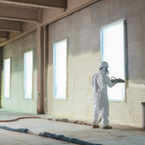worker in safety gear sprays insulation onto a wall
