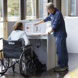 Woman in wheelchair being shown an accessible sink by a standing man