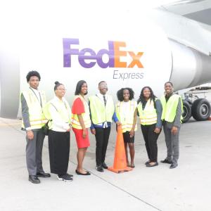 A group of people wearing hi-viz vests while stood next to a FedEx Express aeroplane 