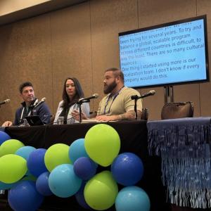 Panelists sat at a table that has green and blue balloon attached to the front 