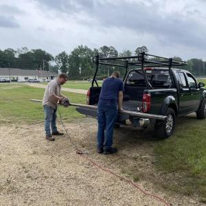 Two people cutting materials on the back of a car trunk 