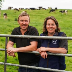 two people leaning against a fence with cows in the background