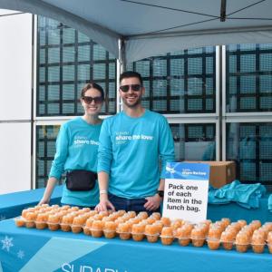 Two people standing behind a table with food items on it