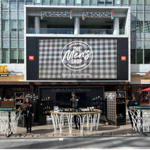 A view of "The Men's Shop" from outside, with people standing by tables