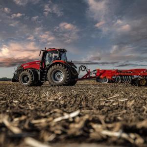 A red tractor in a field with cloudy sky behind it
