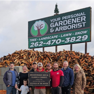 A group of people posing in front of a sign: "Your Personal Gardener & Arborist"