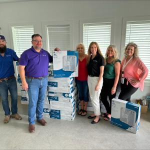 People standing next to stacks of new fans in boxes
