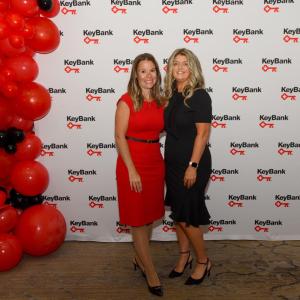 Two people standing together next to a column of red and black balloons, with a KeyBank backdrop
