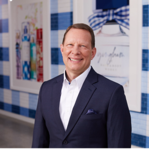 Jeff King stands smiling at the camera in front of a wall painted with a blue and white gingham pattern at Bath & Body Works’ home office in Columbus, Ohio.