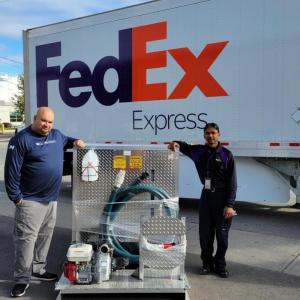 Two people standing next to a FedEx truck with a delivery of equipment