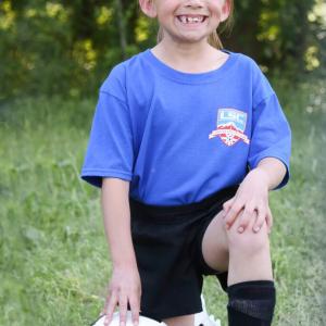 A child kneeling on grass with their hand on a soccer ball
