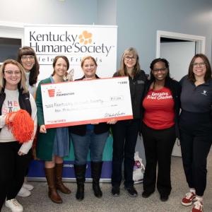 People standing together inside, two of them holding a large check