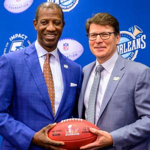 Two people in suits holding the same football and smiling