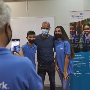 Pep Guardiola poses for a picture with two people wearing Xylem shirts