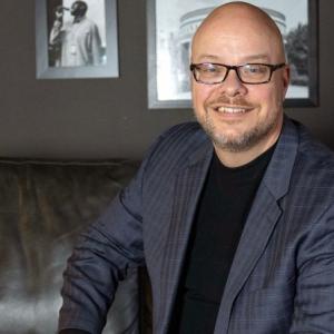 Andy Smith in a gray suit, sitting on a dark sofa