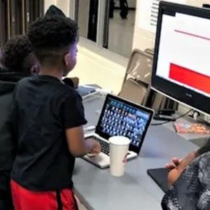 APP YOUniversity students huddle around laptops and a computer monitor