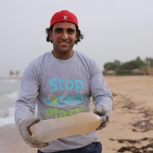 Person standing on beach holding a plastic bottle