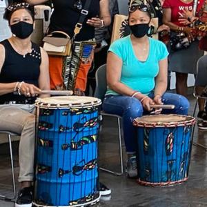 museum-goers in masks sitting behind drums of different colors and sizes