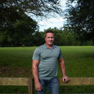 Slade Williams in a green shirt standing in front of a stockade fence