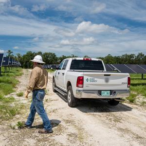 Duke Energy employee in a hardhat inspecting solar panels in a grassy field